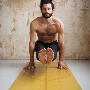 A man balancing in an advanced arm-supported yoga pose on a yellow yoga mat with alignment line markings