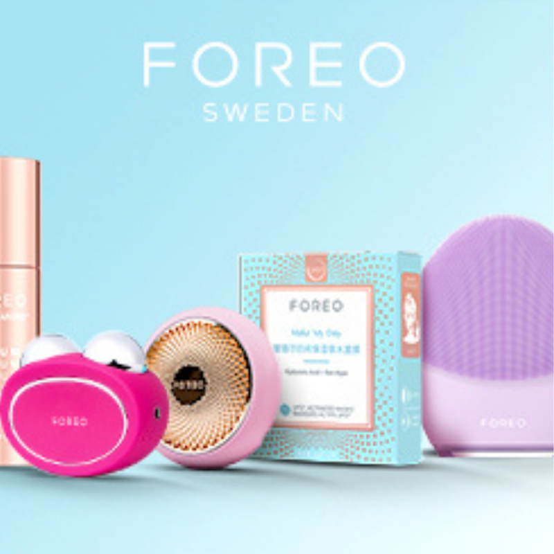 A collection of FOREO Sweden smart skincare devices on a light blue background, featuring a SERUM SERUM SERUM bottle, a hot pink BEAR microcurrent device, a pink UFO mask device with a "Make My Day" face mask box, and a Lavender LUNA facial cleansing brush.