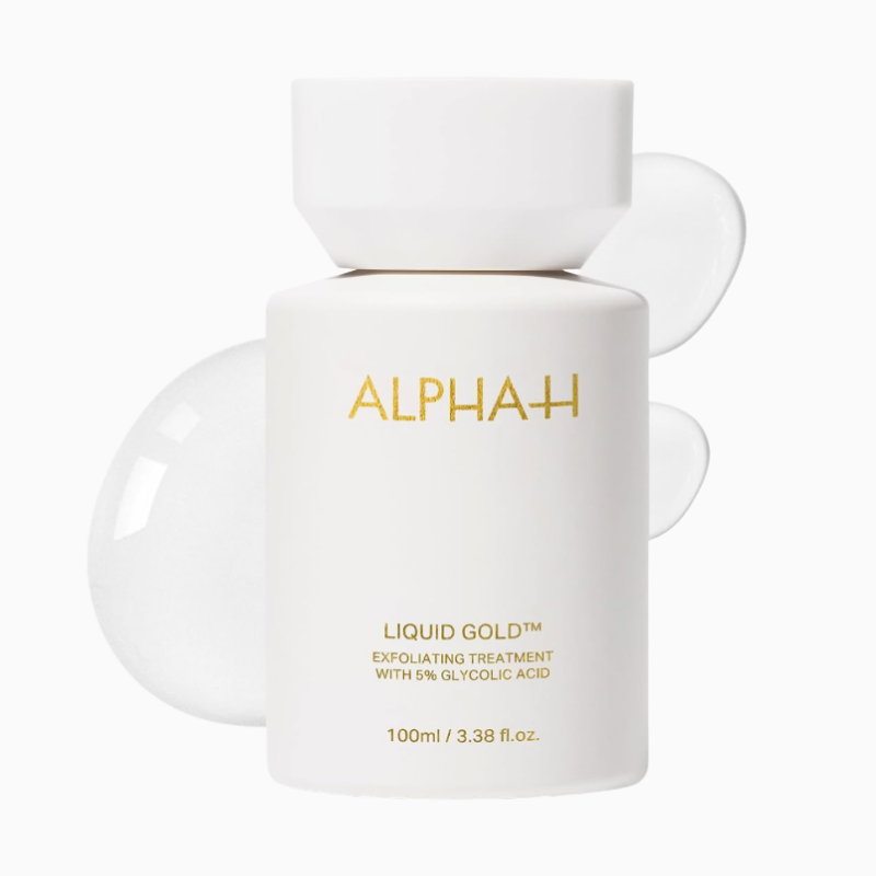 Alpha-H Liquid Gold Exfoliating Treatment bottle centered against a crisp, white background. The elegant, matte white opaque bottle features clean, metallic gold lettering displaying the brand name and the 5% glycolic acid formula details. A glossy, transparent liquid swatch curves smoothly right behind the container, highlighting its weightless fluid texture.